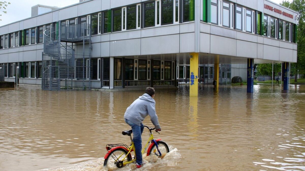 Ein Junge fährt auf dem Fahrrad durch hohes Wasser, welches sich vor einer Schule gesammelt hat.