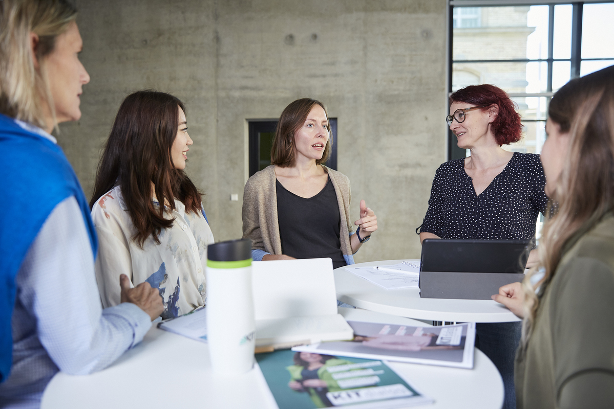 Fünf Frauen stehen am Tisch und diskutieren