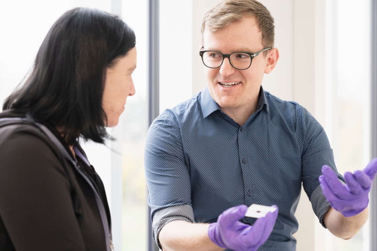 Gabi Zachmann und Cedric Großelindemann im Gespräch, Cedric Großelindemann trägt lila Handschuhe und hält ein kleines Objekt.