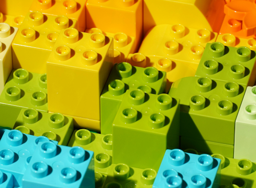 Bunte Lego-Bausteine in Gelb, Grün und Blau gestapelt.